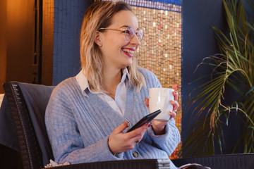 Caucasian woman drinking hot coffee and using technology at a restaurant in France. Cheerful woman calling a friend having tea in the morning working day. Casual lifestyle for young people in Europe.