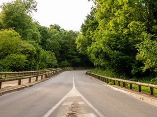 Curved asphalt mountain road through the forest. Wooden railings on the sides.