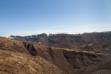 Mountain ridge covered by young, green grass and distant, black mountain cliffs covered by dark, scorched ground after a forest fire