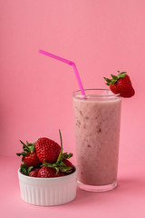 Strawberry milkshake with a pink straw and strawberries on a glass on a pink background. Healthy food and diet concept