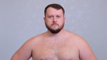 Naklejka premium Portrait of a fat bearded man naked on a torso on a gray background.