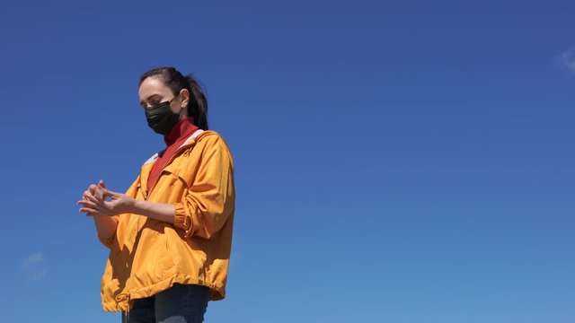 woman puts on a medical mask on a street. blue sky background
