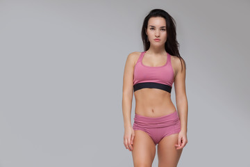 Fototapeta premium Attractive young brunette woman in pink sportswear is posing isolated on grey background