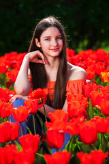 Naklejka premium Young beautiful brunette model posing on a background of red tulips