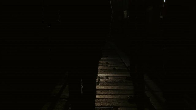 Adult slowly walks moody street in dark alley at sunset, slow motion