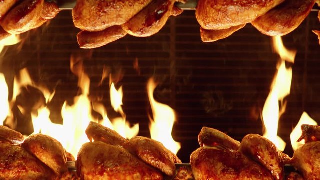 Chickens aligned on spikes  rotate in front of wall of flames in rotisserie