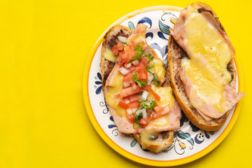 Mexican molletes with ham and cheese on yellow background