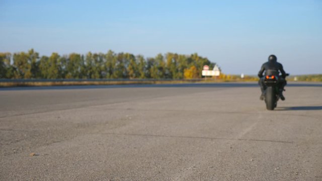 Biker is sitting on his motorcycle at highway and starting ride. Man begin riding a motorbike at country road. Concept of freedom and adventure. Rear view