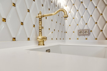 Sink with faucet made of bronze on a white glossy kitchen worktop.