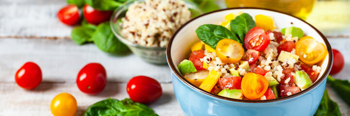 Concept of healthy food, clean eating, low calories delicious meal. Salad with quinoa and fresh vegetables with olive oil in blue bowl. Tomato, avocado, spinach. Close up wooden background, banner