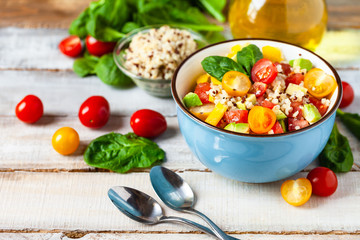 Concept of healthy food, clean eating, low calories delicious meal. Salad with quinoa and fresh vegetables with olive oil in blue bowl. Ripe tomato, avocado, spinach. Close up, wooden background
