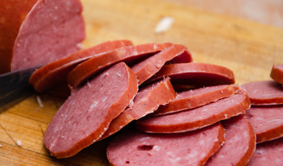 A female hand holds a knife and she cuts sausage on a wooden board. Pizza  sausage