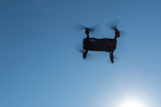 Small sized red drone with high resolution camera hovering in air for aerial photography.