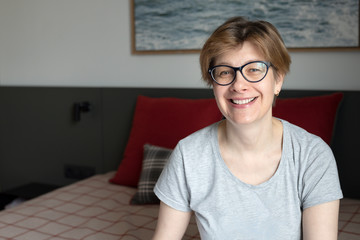 Portrait of a smiling, happy, 50 years old woman. Sits at home on the bed in the bedroom.