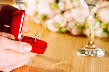 Marriage proposal. Man gives ring with diamond to woman proposing marriage. Indoors restaurant or home, romantic dinner