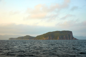 Naklejka premium Island in the sea. Island with steep shores in the sea at sunset.
