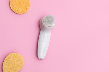 Top view of electric facial brush and face sponges on soft pink background with space for text