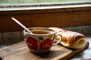 Tea in a painted ceramic cup and a bun on the windowsill. Simple breakfast.