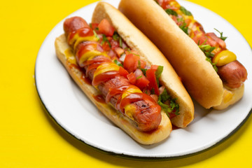Hot dog with pico de gallo salad on yellow background