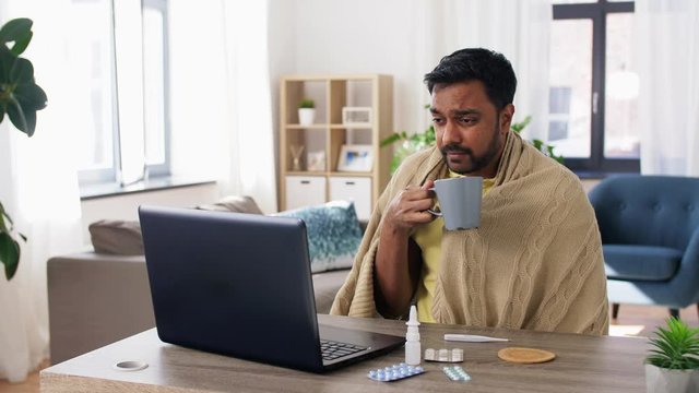 healthcare, technology and people concept - sick indian man in blanket with sore throat having video call or online medical consultation on laptop computer at home