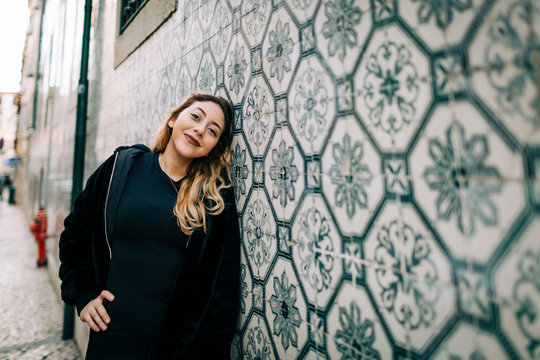Portrait of happy young woman dressed in black leaning against Azulejo wall, Lisbon, Portugal
