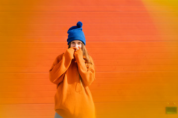 Portrait of teenage girl weraing blue woolly hat and orange sweater in front of orange background