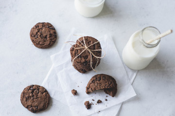 Chocolate cookies with bottles of milk over a rustic paper. 
bird view.