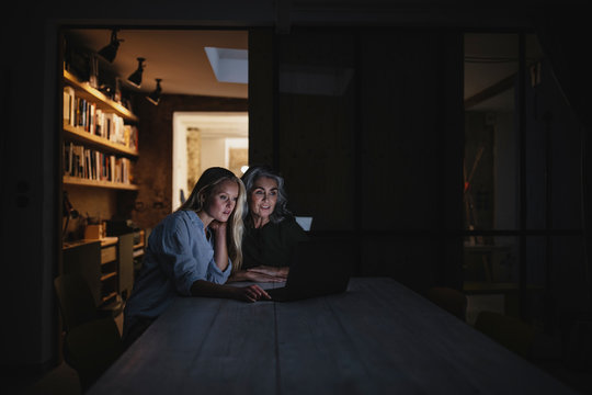 Mother and adult daughter looking at laptop on table in the dark