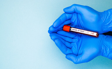 Obraz premium male hands in blue medical gloves hold an ampoule of blood with a positive test for covid-19. passing a test for the presence of coronavirus, space for text