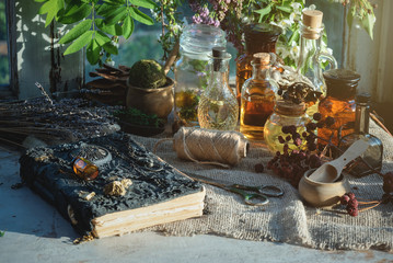 Recipe book, magic potions bottles and dried herbs on the witch doctor table.