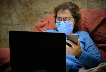 a woman physician homeworking with a notebook and cellphone with a face mask on the couch