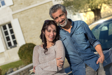 Portrait of happy wealthy middle age couple outside of their house