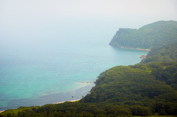 Sea bay in the sea of Japan surrounded by green hills by day.