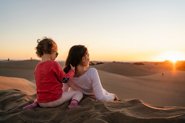 Mother and daughter relaxing in sand dunes at sunset, Gran Canaria, Spain