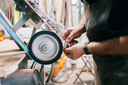 Craftsman making knives in his workshop sharpening the blade - Powered by Adobe