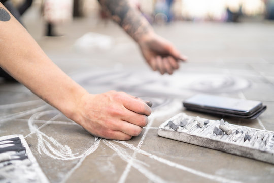 Street art, pavement artist drawing on pavement and using smartphone