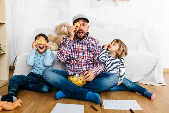 Fahther and children sitting on floor, covering eyes with potatoe chips