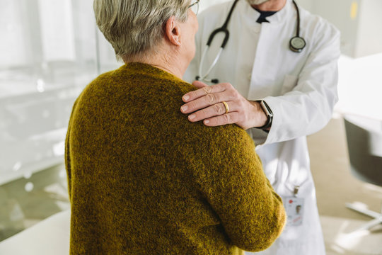 Doctor holding shoulder of senior patient in his practice