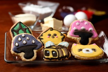 Cookies made with butter and decorated with various figures, in the background in diffuse raw materials for their preparation, mentioning butter, flour, eggs and sugar.