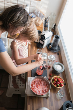 Mother and little daughter preparing strawberry jam in the kitchen at home