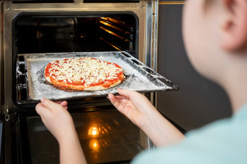 Crop view of boy pushing baking tray with raw pizza in oven