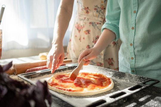Crop view of boy spreading tomato sauce on pizzy base