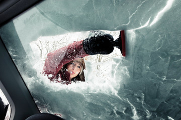 Portrait of young woman cleaning snow from car's windscreen
