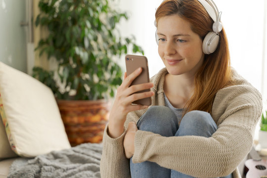 Young woman wearing headphones and using smartphone at home