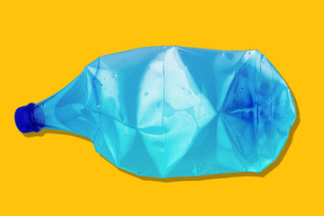 crushed blue plastic bottle on yellow background