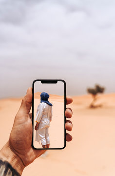 Hand holding smartphone with foto of man walking in the desert
