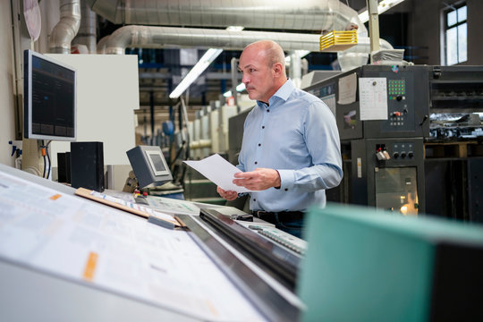 Businessman holding paper at a machine in a factory