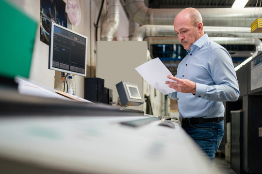 Businessman holding paper at a machine in a factory