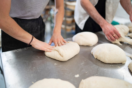 Close-up of man and woman preparing little loaves of bread in bakery