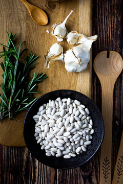 Cutting board, wooden ladle and spoon, garlic, rosemary and bowl of white beans